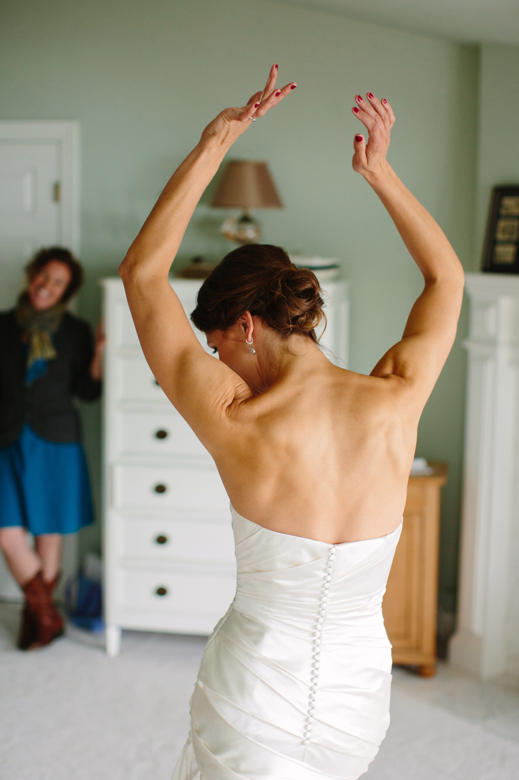 Photo of the bride, Sandra, from behind in her wedding dress with her arms up in the air.