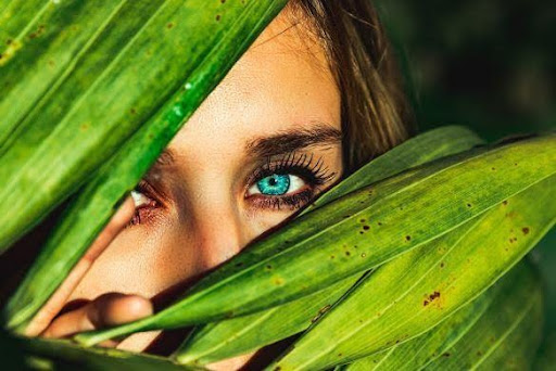 Face of with captivating green eyes behind jungle leaves