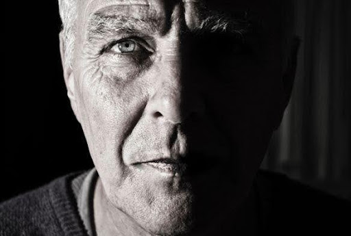 Black and white half in shadow photo of older man with captivating eyes and intense look on his face