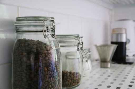 Photo of kitchen counter with mason jar full of coffee beans, and a coffee grinder in the background.